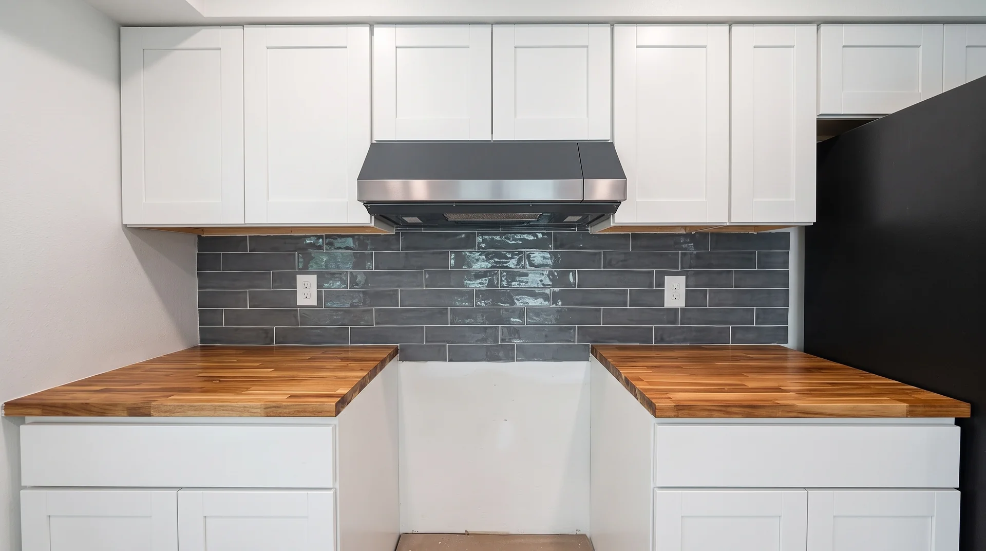 Gray subway tile backsplash between white shaker cabinets and butcher block countertops